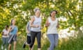 A small group of mature adults are seen running together on a sunny summer evening. They are each dressed comfortably in athletic wear and have smiles on their faces as they spur each other on.