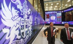 Men walk past information screens at the London Stock Exchange in the City of London which show the FTSE 100 index