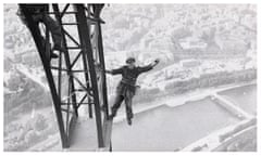 Construction worker showing off by hanging precariously from a metal scaffold high above a city