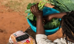 A mobile phone charged using M-Kopa solar technology rests on loaf of bread as a girl prepares food in a basin in Ndela village, Machakos county in Kenya, on July 22, 2015. Customers agree to pay for the solar panel with regular instalments which M-Kopa, a Nairobi-based provider of solar-lighting systems, then monitors for payments that are made using a mobile-phone money-transfer service. 