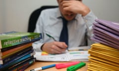 A school teacher holds his head in his hands as he marks papers.