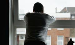 A teenage boy looks out of a bedroom window at the houses in front