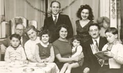 George Szirtes, holding a book, is one of four children sitting  with six adults at a table, with balloons and paper chains on the wal,  in 1957