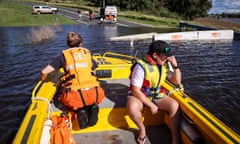 A local sits next to Alex Varley, a member of the NSW SES, as he is transported by boat across a road blocked by flood waters in Rosebrook, north of Maitland