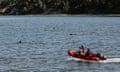 Three people on a bright orange motorboat move across water toward fins.