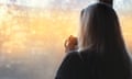 Woman standing by the window, with coffee cup in hands, looking out into the morning light