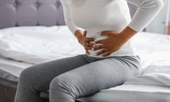 A woman sits on the side of a bed holding her stomach