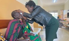 An African woman examines the eyes of a gaunt elderly woman wearing a traditional blanket