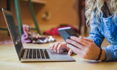 Midsection of female blogger using laptop and smart phone while lying on floor in bedroom