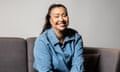 Shani Gonzales in a dsenim jacket smiles for a portrait sitting on a sofa