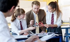 Teacher guiding high school students assembling molecule model in science class