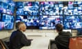 Two staff members sitting at a desk looking up at a bank of CCTV display screens