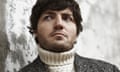 Tom Burke leaning on a weathered wall