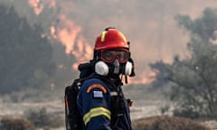 A firefighter in a gas mask faces the camera with flames burning in background