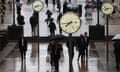 People walk beneath clocks that are part of the Six Public Clocks artwork