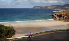 Nell Nelson on her bike on a road curving round and down, overlooking Whiten Head