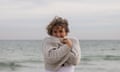 Woman stand on windy beach holding her beige cardigan wrapped around her