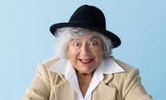 Actor Miriam Margolyes in white shirt, beige jacket and black hat, against blue background