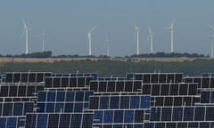Photovoltaic power panels stand at Abaste’s El Bonillo Solar Plant while wind turbines spin at a wind farm on the background in Albacete province, Spain.