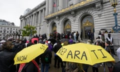 A crowd outside city hall with yellow umbrellas with 'reparations now' printed on them.