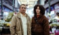 Robert, played by Cliff Curtis and Elsie, played by Tanzyn Crawford pose with a serious expression, looking down the barrel of the camera in front of a flower market.