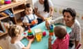 A nursery teacher plays with three young children around a low table