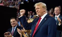 white man wearing blue suit and red tie holds fist up in air