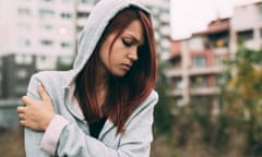 Teen girl in hoodie, looking sad, standing alone outdoors