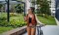 Portrait of young urban woman drinking coffee while walking alongside her bicycle.