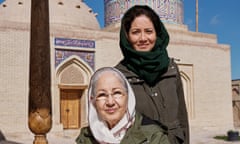 Mishal Husain, wearing a green headscarf and coat, and standing next to her mother, Shama, who is also wearing a coat and headscarf, and sitting on an upholstered bench outside a domed and decorated mausoleum