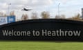 A plane flies over a sign that reads ‘Welcome to Heathrow’