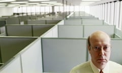 Businessman standing in cubicle in empty office, looking unhappy