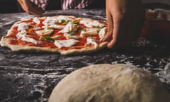 A chef preparing a cheese and basil pizza