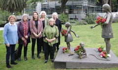 A group of six women standing next to a statue of a young women with small children