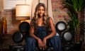 Yewande Biala, with long curly hair and long fingernails and wearing a denim corset, sits on a sofa with round cushions