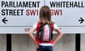 Young girl standing facing a road sign pointing to Whitehall and Parliament Street.