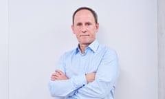 Darius Hughes stands with his arms folded for a portrait in shirt and jeans against a pale background