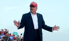 a man in a suit with a red baseball cap speaks with his hands outstretched