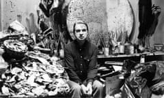 Black and white portrait of Francis Bacon in his studio, surrounded by debris and materials, staring fixedly at the viewer