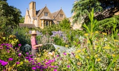 An explosion of blooms, being watered by a woman gardener in a hat, frame the manor house at Hidcote