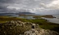 Canna advertises for new population<br>Looking view out to sea across rocks from the island of Canna; grassy slopes stretch down to the water and the islands of Rum and Sanday can be seen in the distance. The sky is grey and cloudy, and the sea dark.