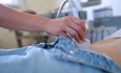 A hand holds an ultrasound scanner on a woman's lower torso.