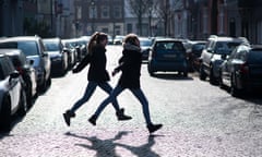 Two school-age girls skipping across a street in a city