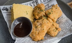 Fried vegan tenders served on a newspaper-lined plate with cornbread and barbecue sauce.