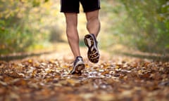 The legs of a runner on a path covered with autumn leaves