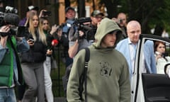 Man in green hoodie being filmed by media near open car