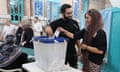 A man and a woman with loose headscarf put their vote in a box