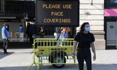 A woman walks passed a sign advising people to wear face coverings outside Victoria station in central London