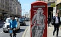 Man on a bicycle passing graffiti poster of Einstein on a bike on a red phone box in the Strand, London