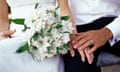 A bride and groom touch hands while the bride holds a bouquet of white lilies.